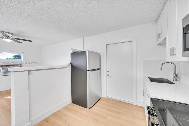 kitchen with sink, light hardwood / wood-style flooring, stainless steel fridge, stove, and white cabinets