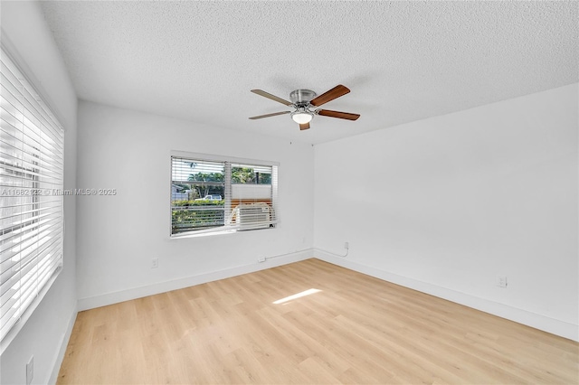 empty room with ceiling fan, light hardwood / wood-style floors, a textured ceiling, and a wealth of natural light