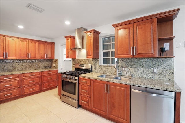 kitchen with wall chimney range hood, light stone counters, backsplash, sink, and stainless steel appliances