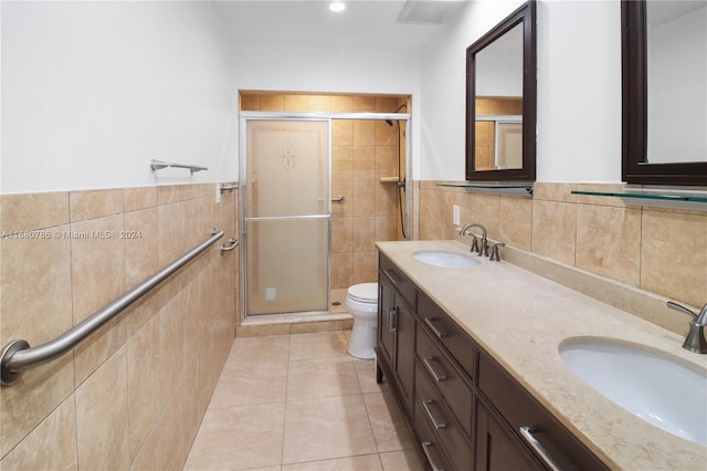 bathroom featuring a shower with shower door, toilet, tile walls, vanity, and tile patterned flooring