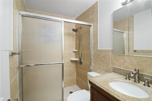 bathroom with decorative backsplash, toilet, a shower with shower door, vanity, and tile walls