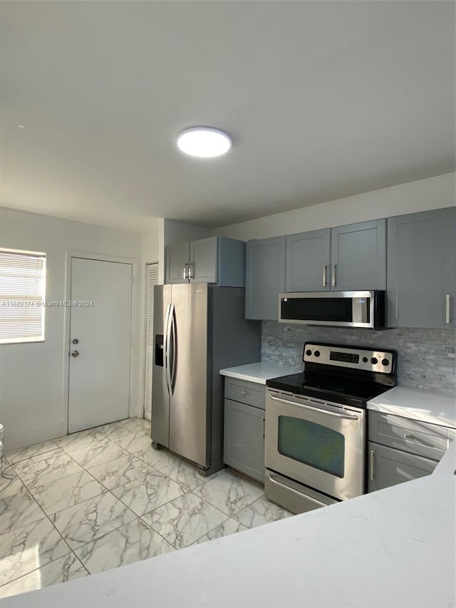 kitchen with appliances with stainless steel finishes, gray cabinets, and backsplash