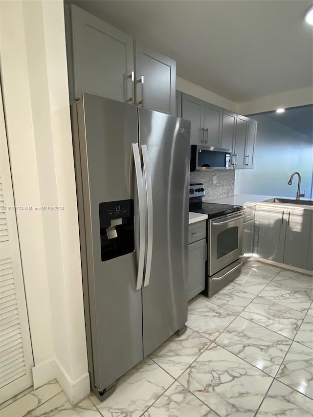 kitchen with gray cabinets, stainless steel appliances, sink, and backsplash