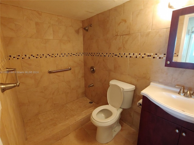 bathroom featuring toilet, tile patterned flooring, vanity, tile walls, and a tile shower