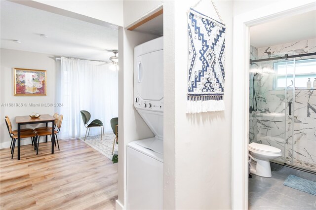 interior space with hardwood / wood-style floors, ceiling fan, toilet, walk in shower, and stacked washer and clothes dryer