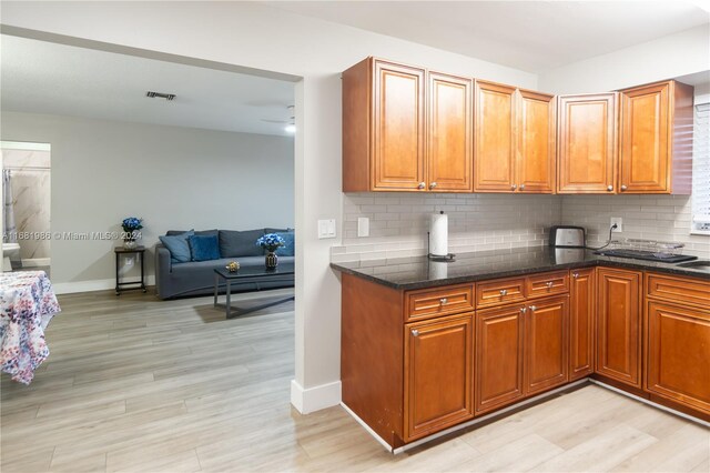 kitchen with light hardwood / wood-style flooring, tasteful backsplash, and dark stone counters