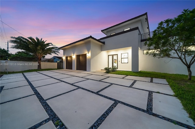 back house at dusk featuring a garage, a balcony, and a patio