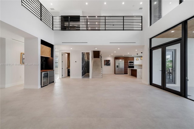 unfurnished living room with french doors, a towering ceiling, and beverage cooler