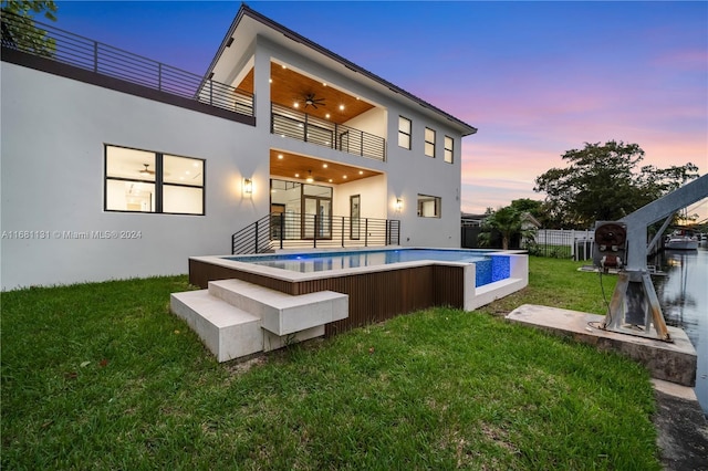 back house at dusk featuring a yard, a balcony, and ceiling fan