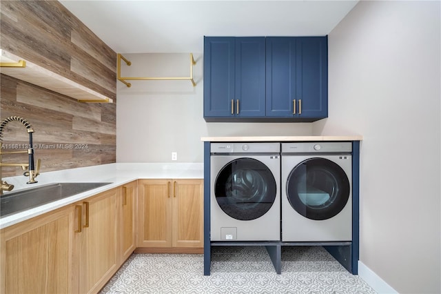 clothes washing area with washing machine and dryer, wood walls, sink, and cabinets