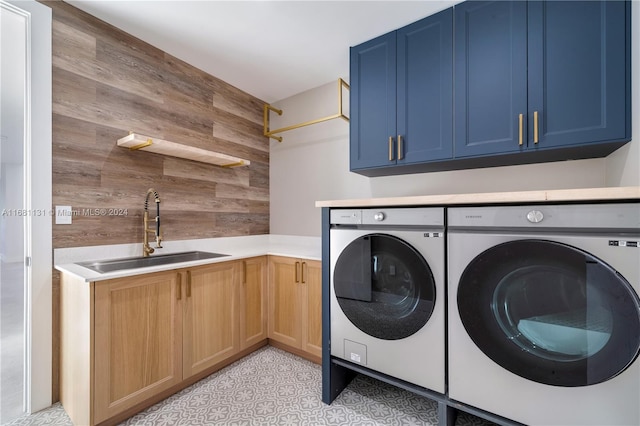 clothes washing area with wood walls, cabinets, independent washer and dryer, and sink