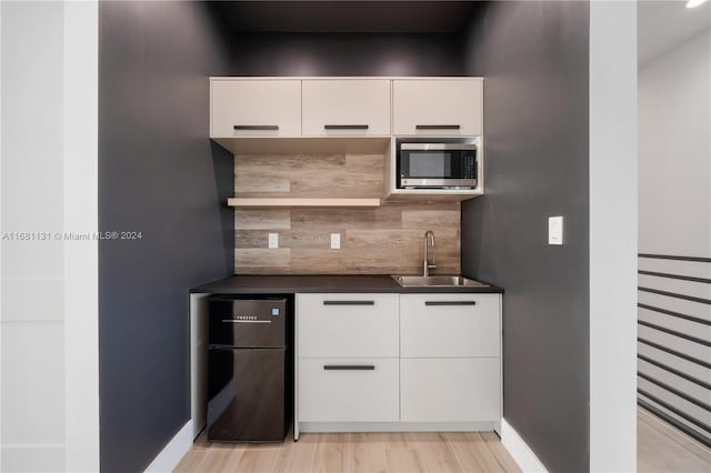 kitchen with black fridge, sink, white cabinets, and light hardwood / wood-style flooring