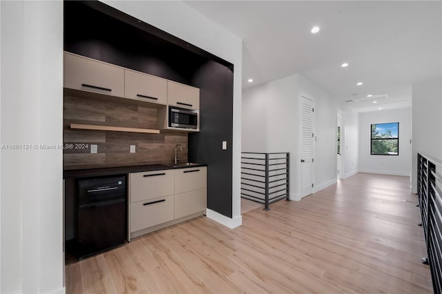 kitchen featuring stainless steel microwave, sink, decorative backsplash, light wood-type flooring, and cream cabinetry