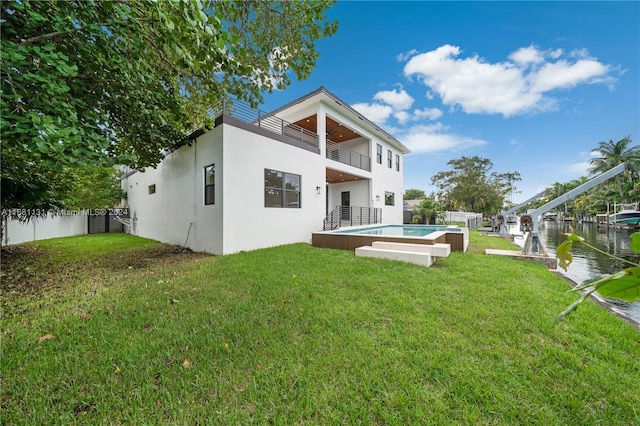 back of house with a balcony, a water view, and a lawn