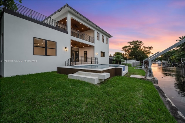 back house at dusk with a lawn, a balcony, and a hot tub