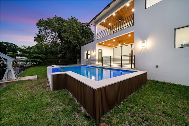 pool at dusk with ceiling fan and a yard