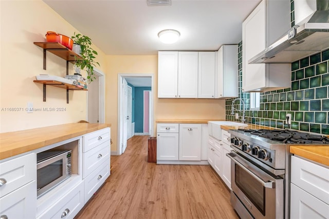 kitchen featuring wall chimney exhaust hood, appliances with stainless steel finishes, butcher block countertops, and white cabinets