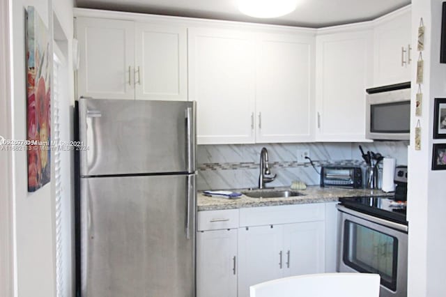 kitchen featuring white cabinets, backsplash, light stone countertops, sink, and stainless steel appliances