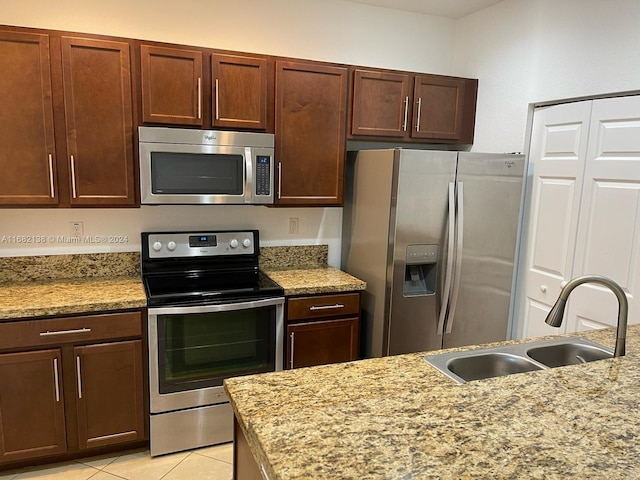 kitchen with appliances with stainless steel finishes, light tile patterned flooring, light stone countertops, and sink