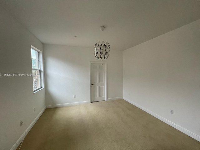 carpeted spare room featuring a chandelier