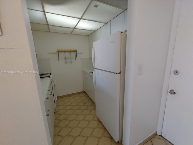 kitchen featuring white fridge, a drop ceiling, and white cabinets