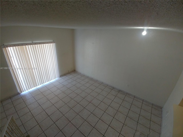 tiled empty room with lofted ceiling and a textured ceiling