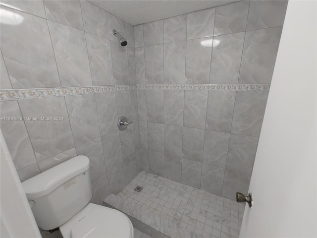 bathroom with a tile shower, toilet, and tile walls