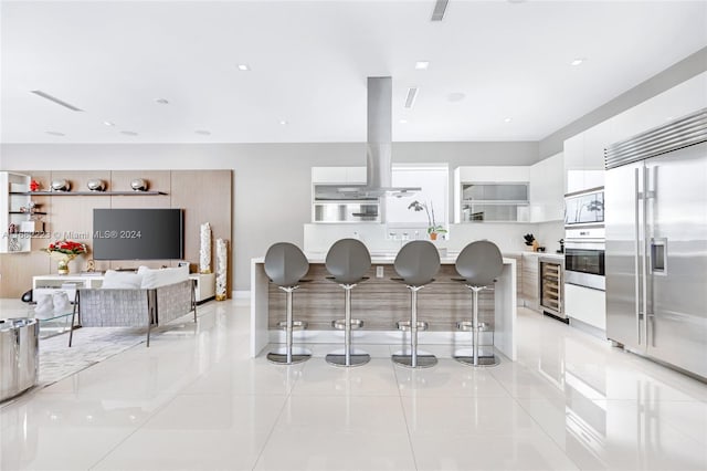 kitchen featuring wine cooler, white cabinetry, built in appliances, and a breakfast bar area