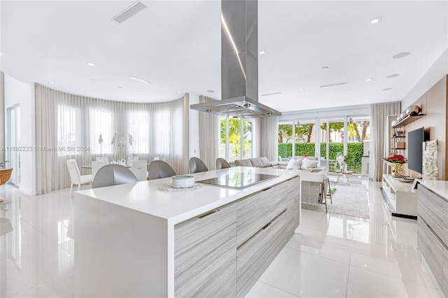 kitchen featuring island range hood, a spacious island, black electric cooktop, a kitchen breakfast bar, and light tile patterned floors