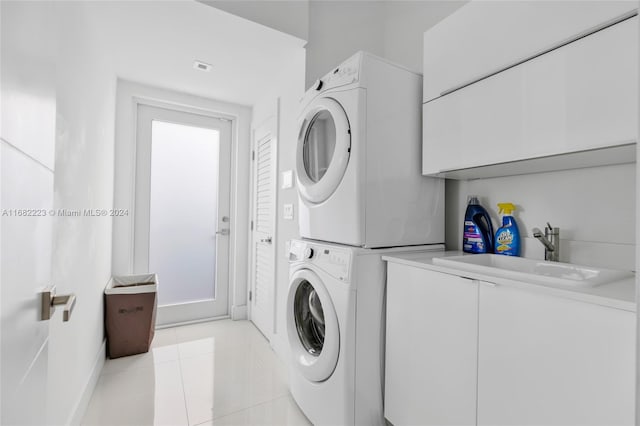 laundry room featuring sink, stacked washer and clothes dryer, light tile patterned floors, and cabinets