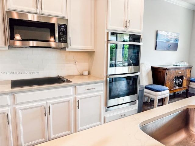 kitchen featuring appliances with stainless steel finishes, backsplash, white cabinetry, light stone counters, and ornamental molding