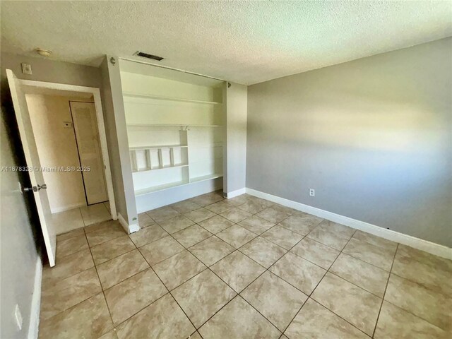 spare room with a textured ceiling, light tile patterned flooring, and built in shelves