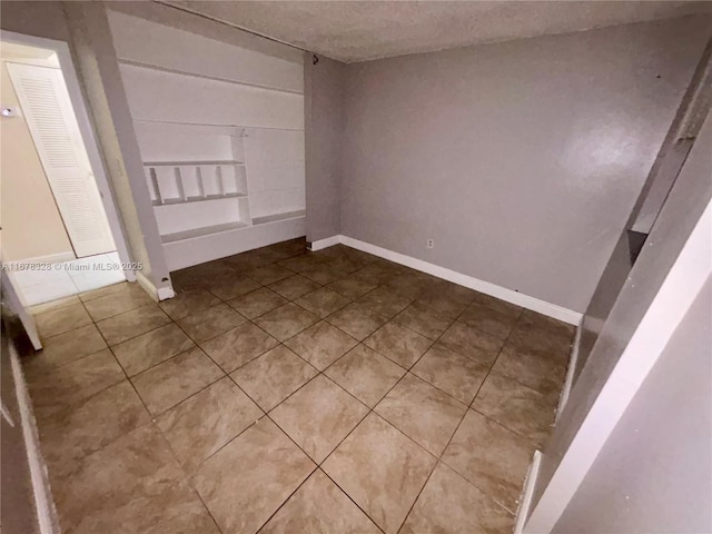 tiled spare room with a textured ceiling and built in shelves