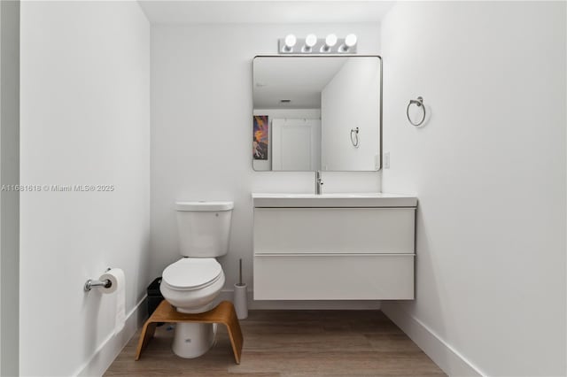 half bathroom with vanity, wood finished floors, toilet, and baseboards