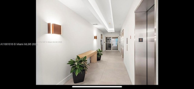 corridor featuring elevator, baseboards, light tile patterned floors, and visible vents