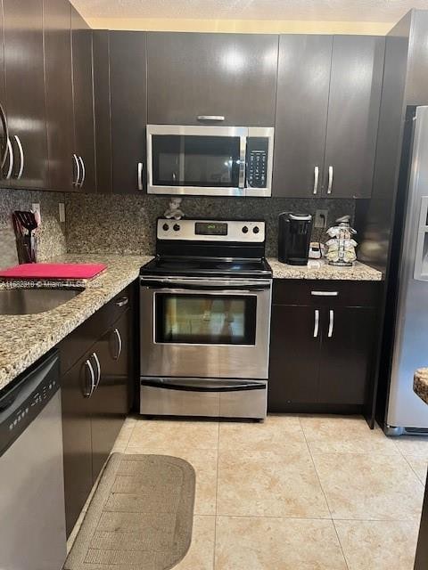 kitchen with light stone countertops, dark brown cabinetry, stainless steel appliances, and backsplash