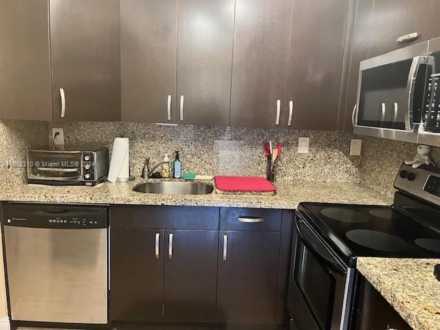 kitchen featuring dark brown cabinets, stainless steel appliances, backsplash, sink, and light stone countertops