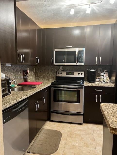 kitchen featuring tasteful backsplash, light stone counters, a textured ceiling, light tile patterned flooring, and stainless steel appliances