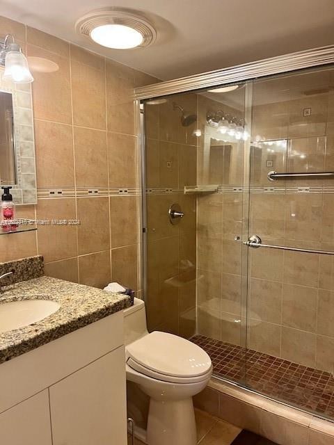 bathroom featuring walk in shower, tile walls, toilet, vanity, and tile patterned flooring