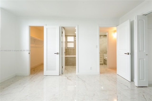 unfurnished bedroom featuring a closet, ensuite bathroom, and a walk in closet