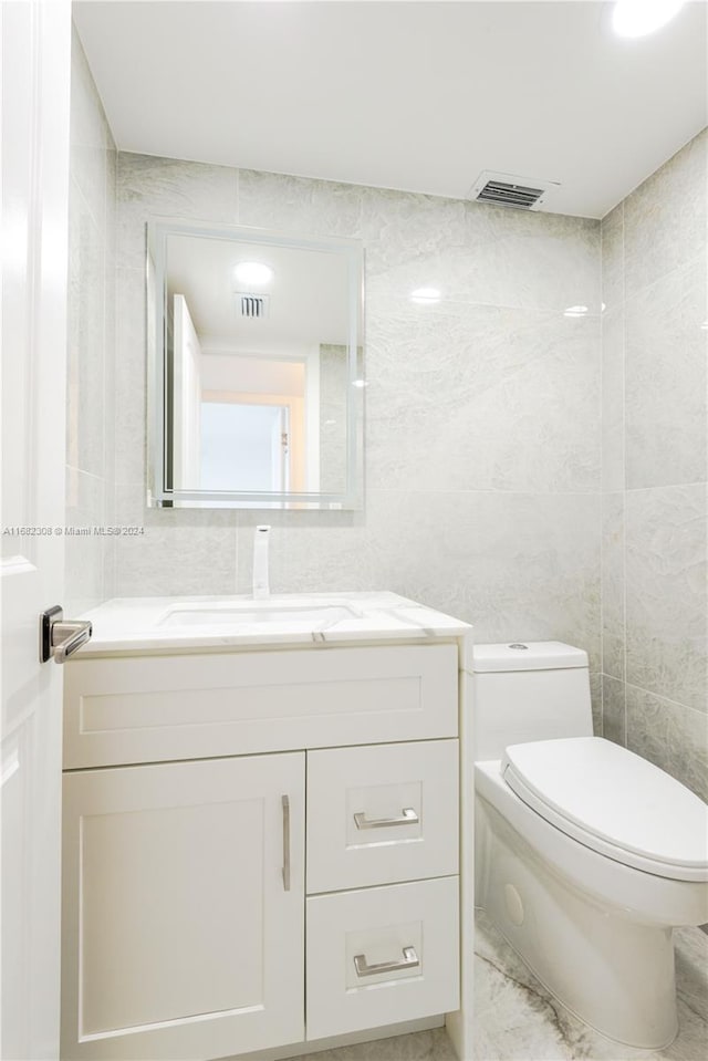 bathroom with vanity, toilet, and tile walls