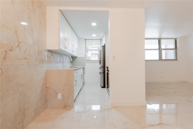 kitchen with tile walls, appliances with stainless steel finishes, sink, and white cabinets