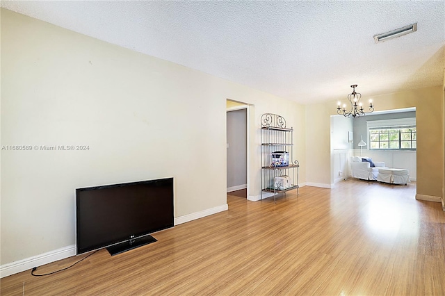 unfurnished living room featuring light hardwood / wood-style flooring, a textured ceiling, and a chandelier