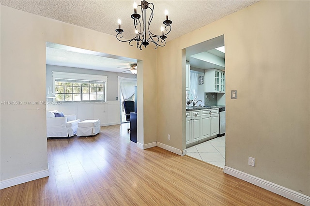 unfurnished dining area with sink, ceiling fan with notable chandelier, a textured ceiling, and light hardwood / wood-style floors