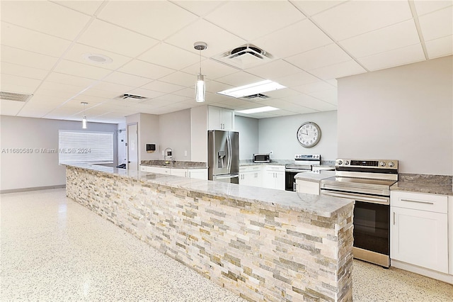 kitchen featuring pendant lighting, white cabinets, stainless steel appliances, and a paneled ceiling