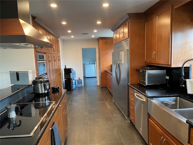 kitchen with wall chimney exhaust hood, washer and dryer, stainless steel appliances, and dark tile patterned flooring