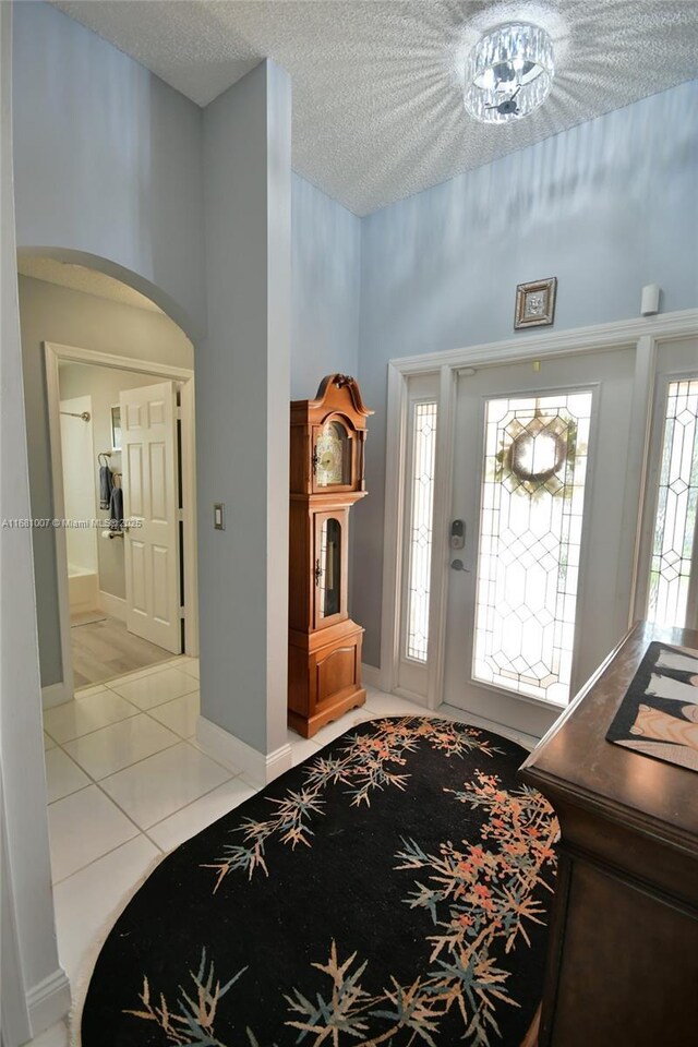 foyer with light tile patterned floors, baseboards, arched walkways, and a textured ceiling