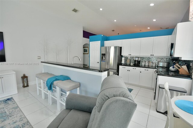 kitchen featuring dark countertops, light tile patterned floors, decorative backsplash, white cabinets, and stainless steel fridge