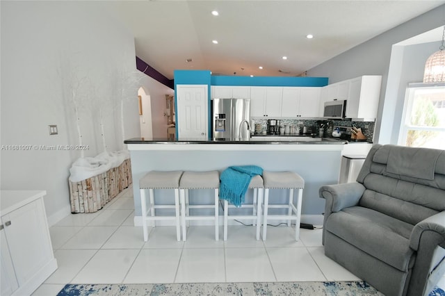 kitchen with backsplash, appliances with stainless steel finishes, a breakfast bar, white cabinetry, and vaulted ceiling