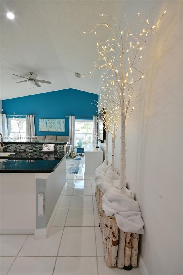 kitchen with dark countertops, lofted ceiling, light tile patterned floors, a ceiling fan, and a sink